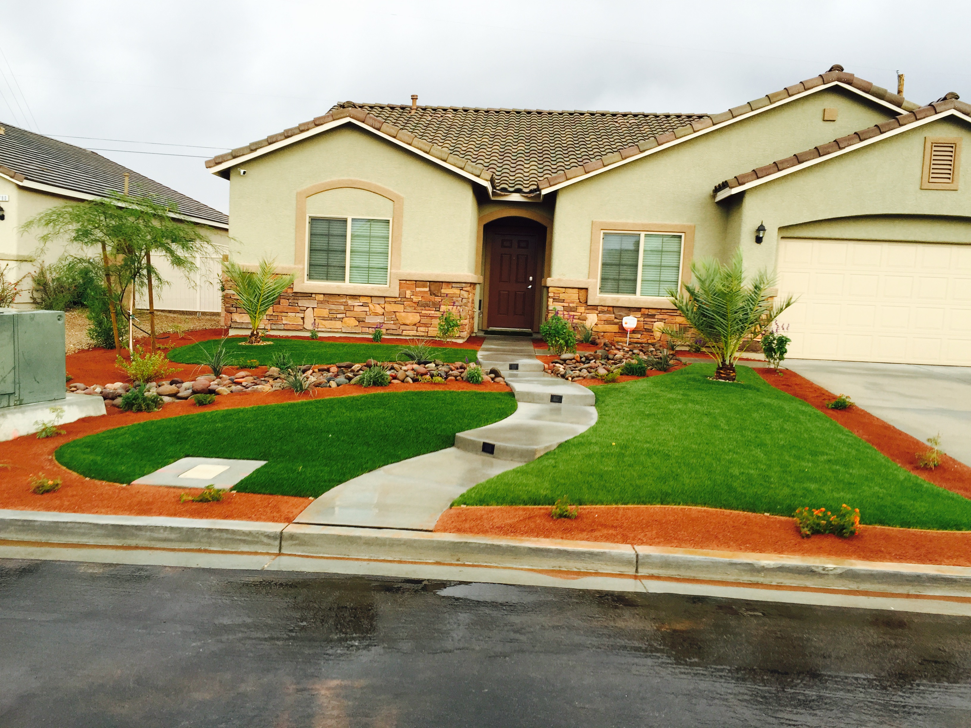 Gorgeous front yard in a suburban neighborhood, including neat grass, natural stones, and local plant life.